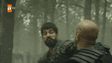 a man with a beard is holding another man 's arm in a forest .