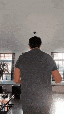 a man in a grey shirt is standing in a living room looking up at the ceiling