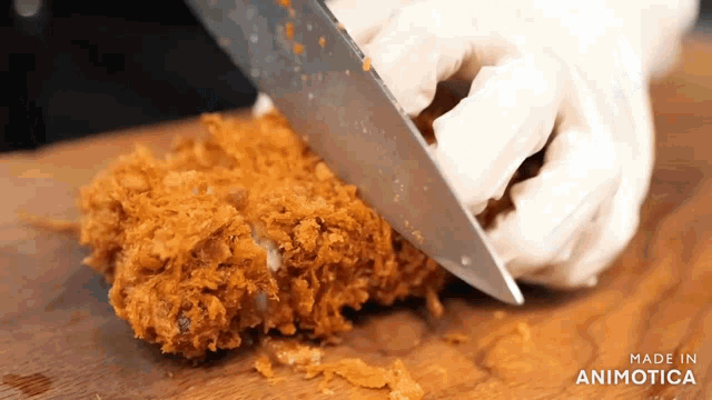 a person is cutting a piece of fried food with a knife on a wooden cutting board ..