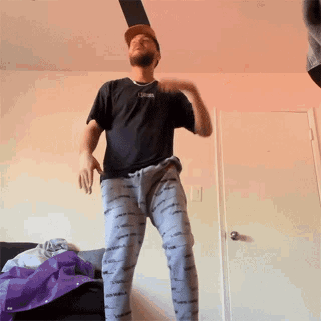 a man wearing a black shirt and grey pants is dancing in a living room