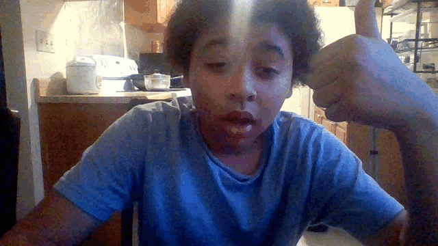 a boy giving a thumbs up in a kitchen