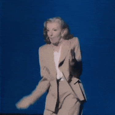 a woman in a tan jacket stands in front of a screen that says ts tech