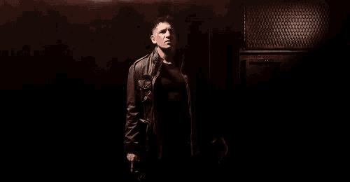 a man in a leather jacket is standing in a dark room holding a gun in his hand .
