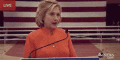 a woman stands at a podium in front of an american flag with the word live on the screen behind her