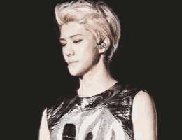 a young man with blonde hair is standing in front of a microphone and wearing ear buds .