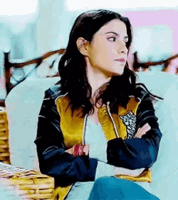 a woman is sitting on a couch with her arms crossed and wearing a yellow and black jacket .