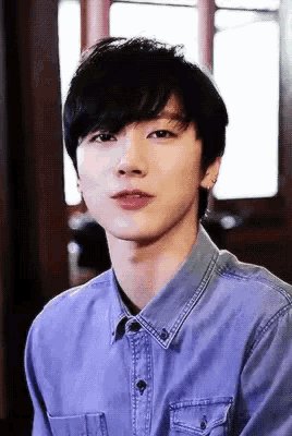 a young man wearing a blue denim shirt is looking at the camera