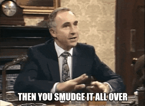 a man in a suit and tie is sitting at a table and says " then you smudge it all over "