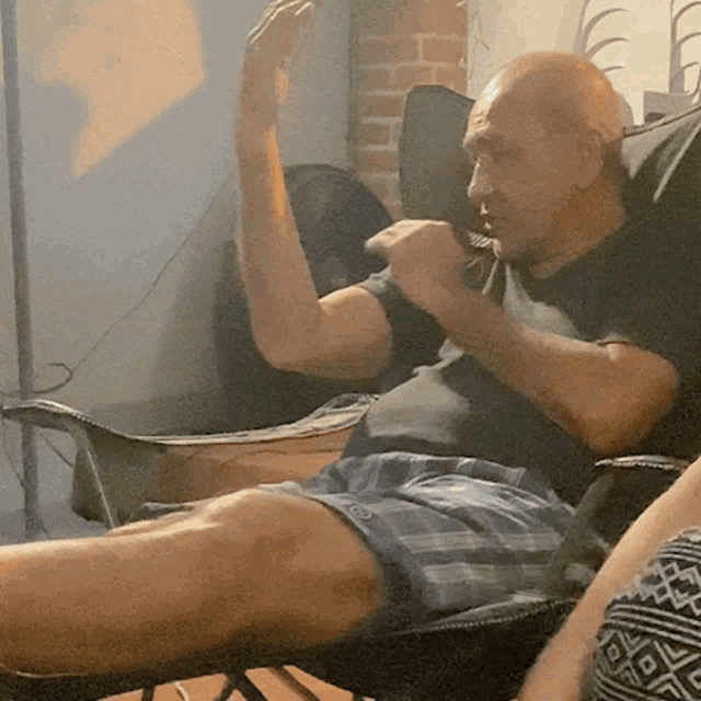 a man in a black shirt and blue shorts is sitting on a chair