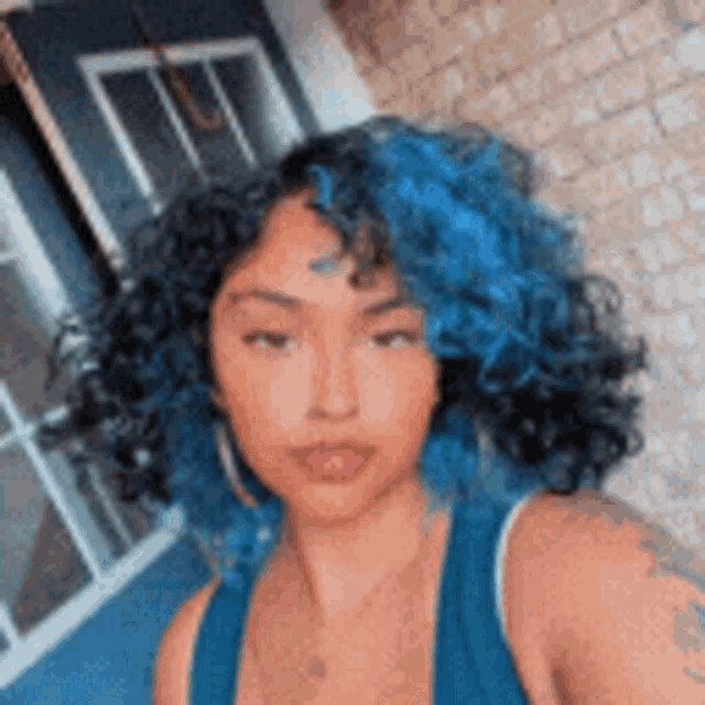 a woman with blue curly hair is taking a selfie .