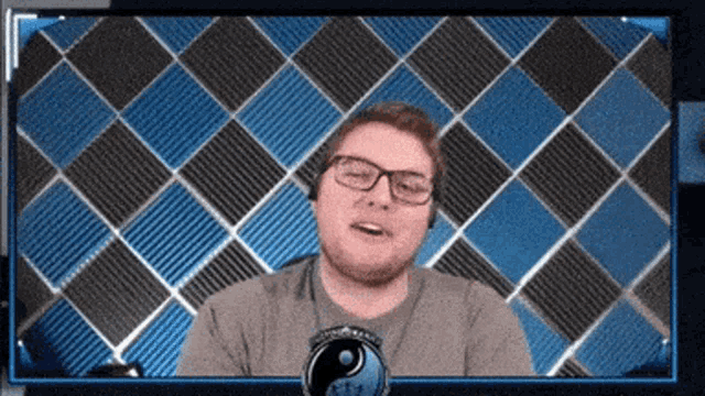 a man wearing glasses is smiling in front of a checkered wall
