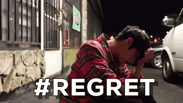 a man in a plaid shirt is sitting on the ground with his head in his hands and the word regret written in white letters