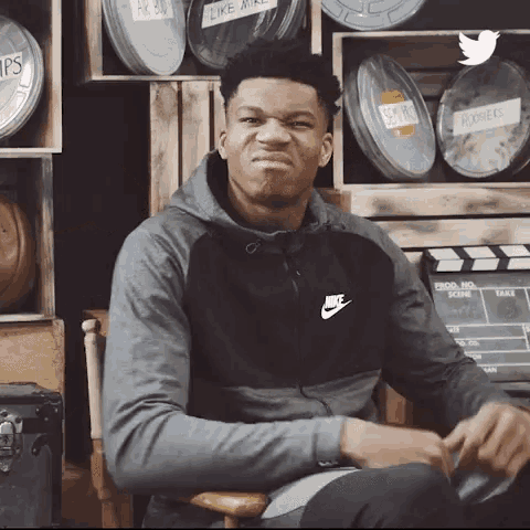 a man wearing a nike sweatshirt is sitting in front of a row of film cans