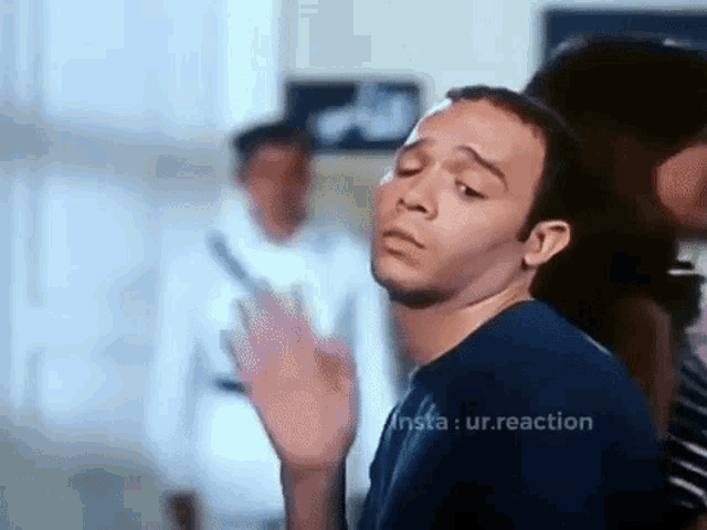 a man in a blue shirt is making a funny face and waving his hand in front of a group of people .