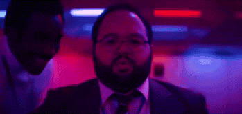 a man with a beard and glasses is standing in front of a red and blue light .