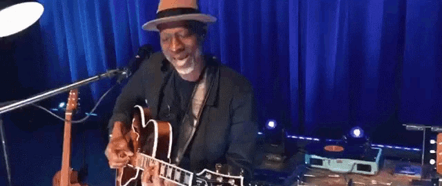 a man is playing a guitar in front of a blue curtain .