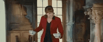 a woman in a red jacket is standing in a room holding two bowls .