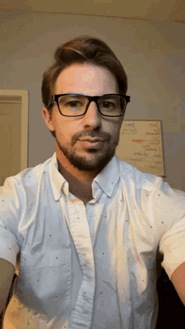 a man wearing glasses and a white shirt takes a picture of himself