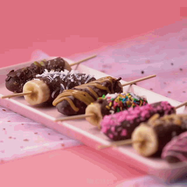 a tray of chocolate covered bananas on sticks with different toppings