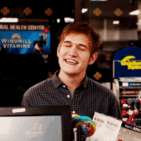 a man in a plaid shirt is smiling in front of a windmill vitamins sign .