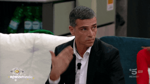 a man in a suit is sitting on a couch in front of a screen that says grandefratello on it