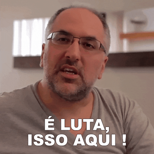 a man wearing glasses and a gray shirt says e luta isso aqui