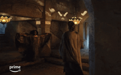 a man in a gray cape stands in a dark room