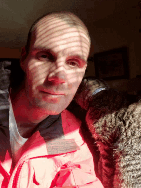 a man wearing a pink jacket holds a cat on his shoulder