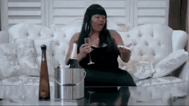 a woman is sitting on a couch holding a glass of champagne and a bottle of champagne .