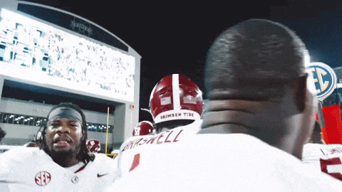 a man wearing a crimson tide jersey is hugging another man