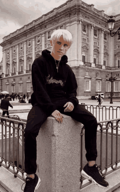a young man in a black hoodie is sitting on a stone pillar in front of a large building