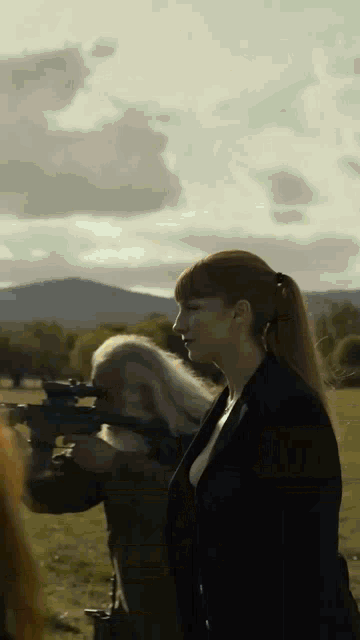 a woman in a ponytail is holding a gun in a field .