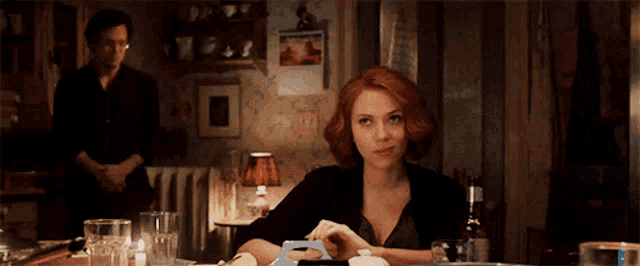 a woman is sitting at a table with a man smoking a cigarette behind her