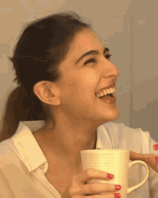 a woman in a white shirt is laughing while holding a white cup