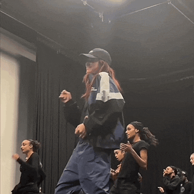a group of people are dancing on a stage and one of them is wearing a nike hat
