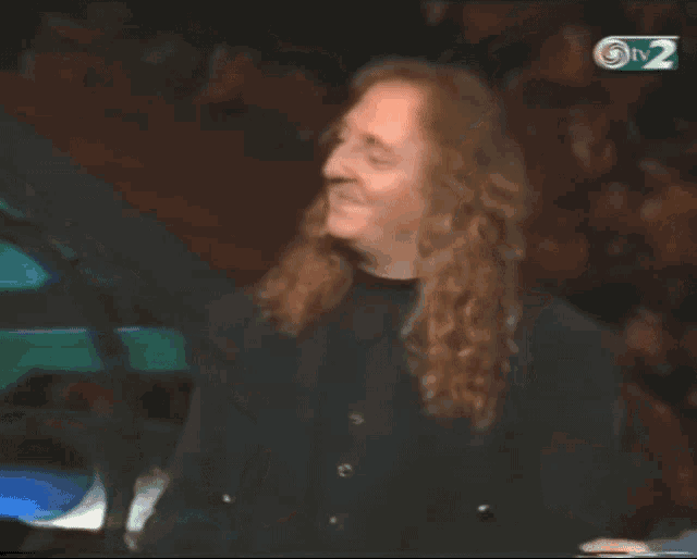 a woman with long red hair is smiling in front of a tv2 sign