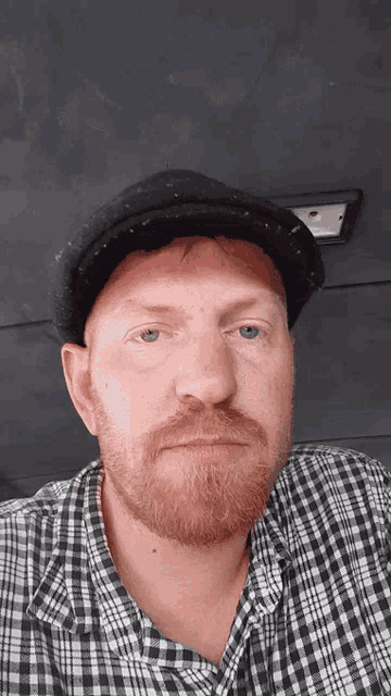 a man with a beard wearing a plaid shirt and a black hat