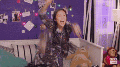 a woman is sitting on a bed with a teddy bear in her room .