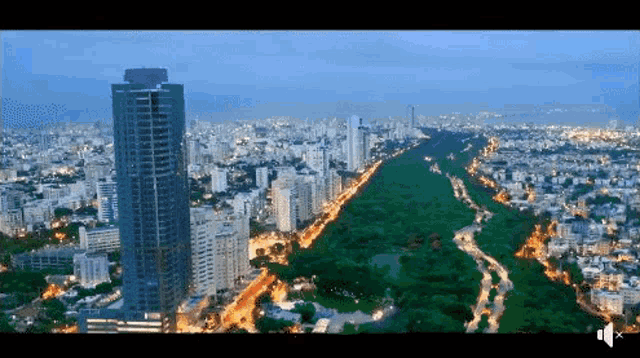 an aerial view of a city at night with a very tall building in the foreground