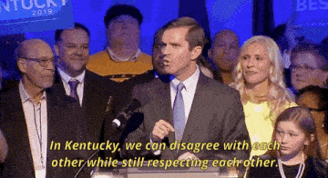 a man in a suit and tie stands at a podium with a crowd behind him and says in kentucky