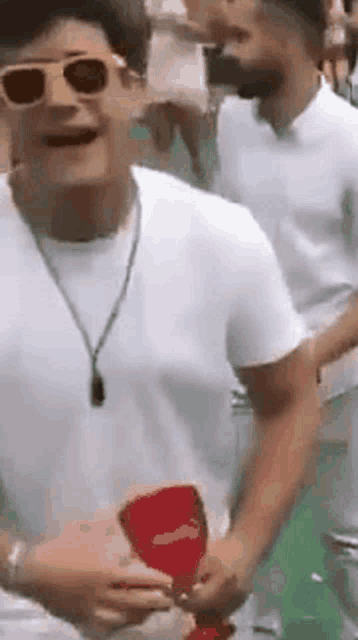 a man wearing sunglasses is holding a red cup .