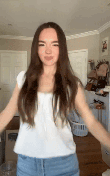 a woman in a white shirt and blue jeans is dancing in a room