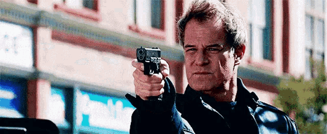 a man is pointing a gun at the camera in front of a building that says domino 's pizza .
