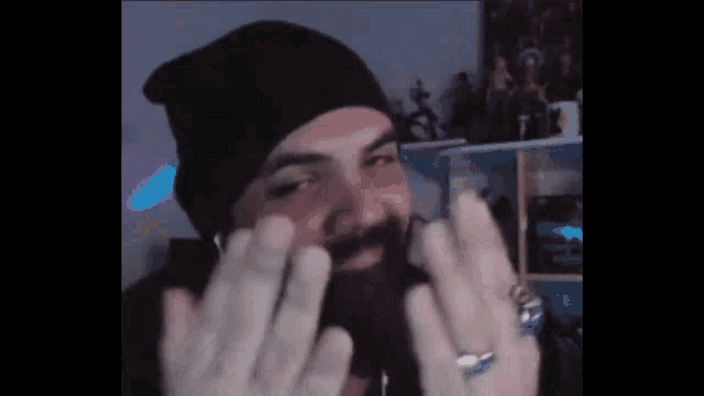 a man with a beard wearing a black beanie and a ring on his finger is making a funny face .