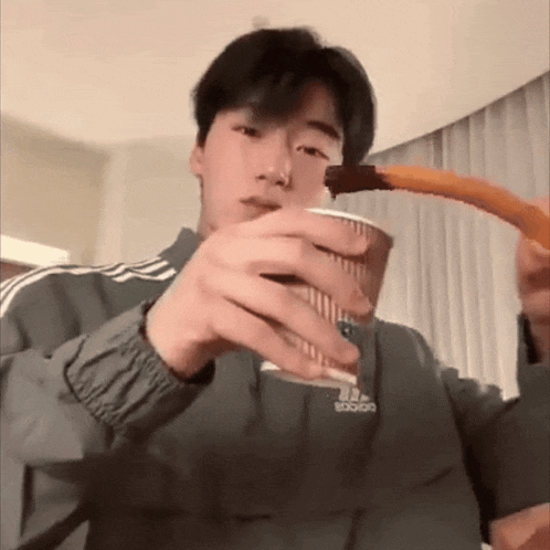 a man wearing an adidas jacket is holding a cup and a churro