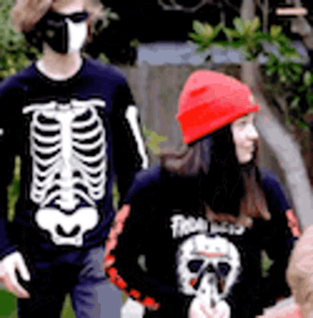 a man wearing a skeleton sweater and a woman wearing a red hat are walking down the street .