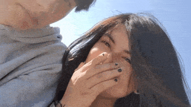a woman is covering her mouth with her hand while a man looks at her .