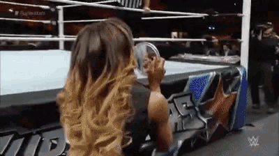 a woman is sitting on the edge of a wrestling ring drinking from a glass .