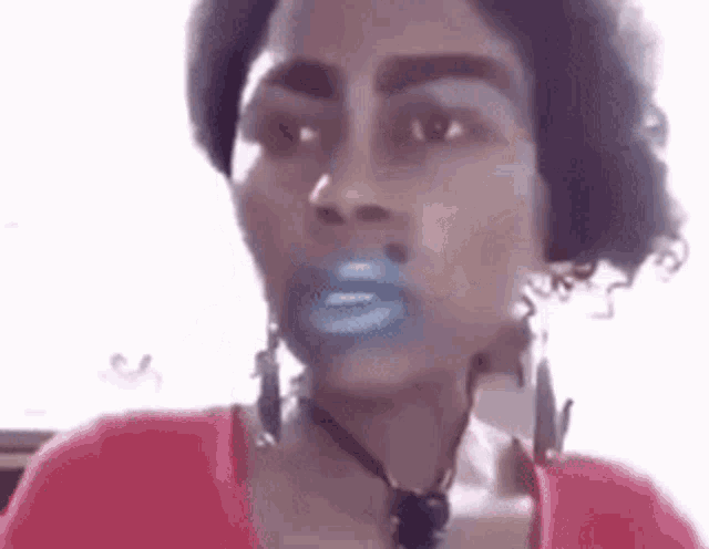 a woman wearing a red shirt and earrings has blue lipstick on her lips .