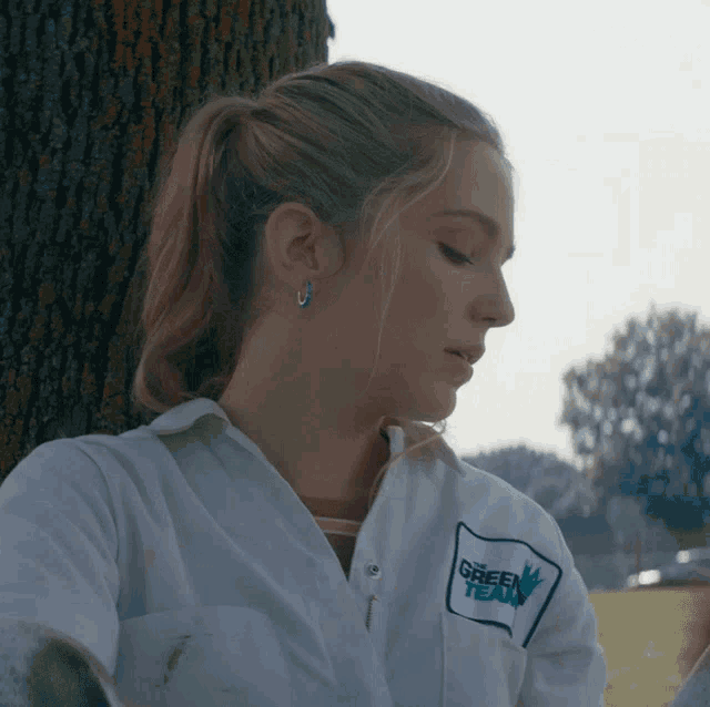 a woman leaning against a tree wearing a shirt that says green tea